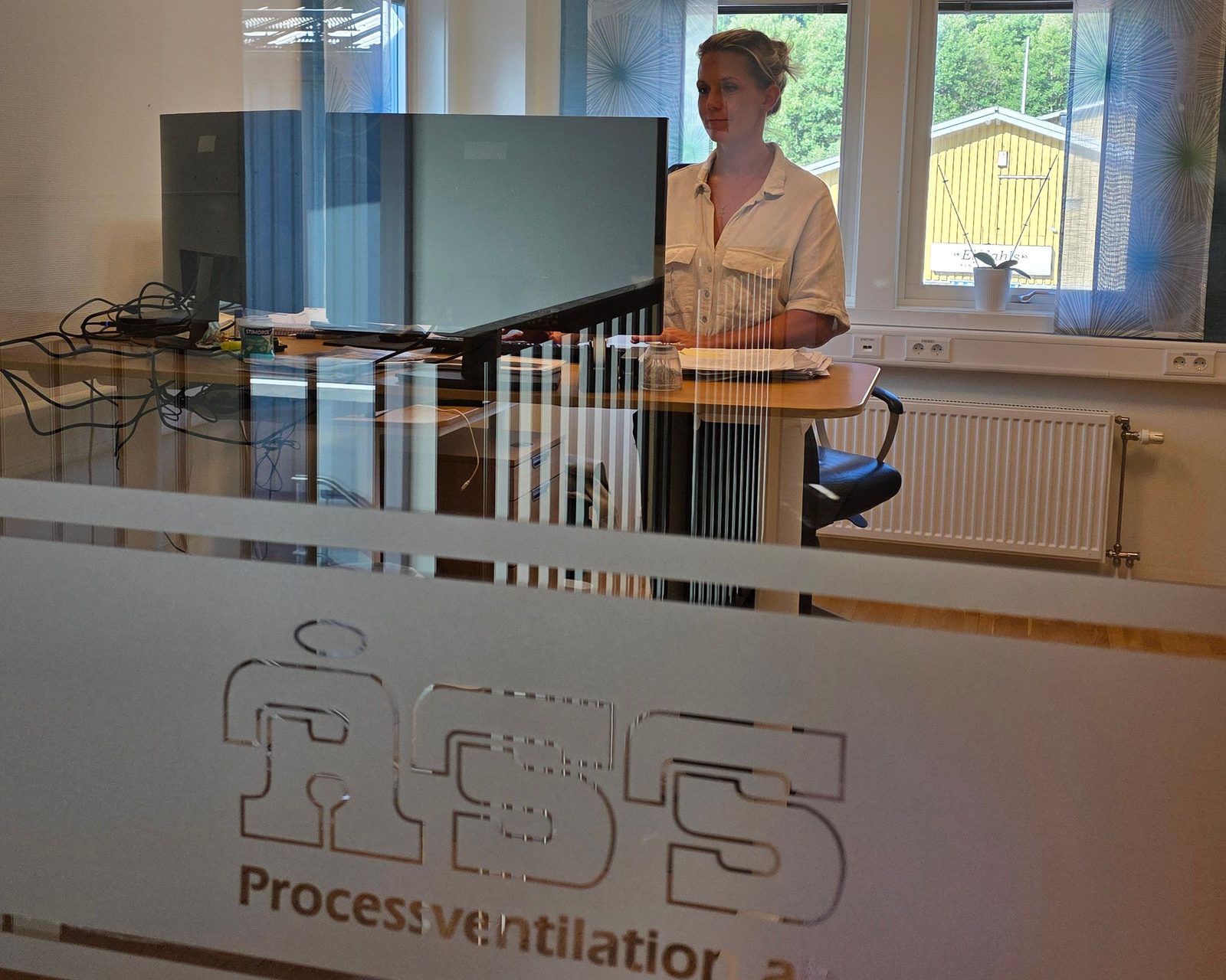 Kontorsrum sett genom en glasvägg med ÅSS Processventilations logotyp etsad i glaset