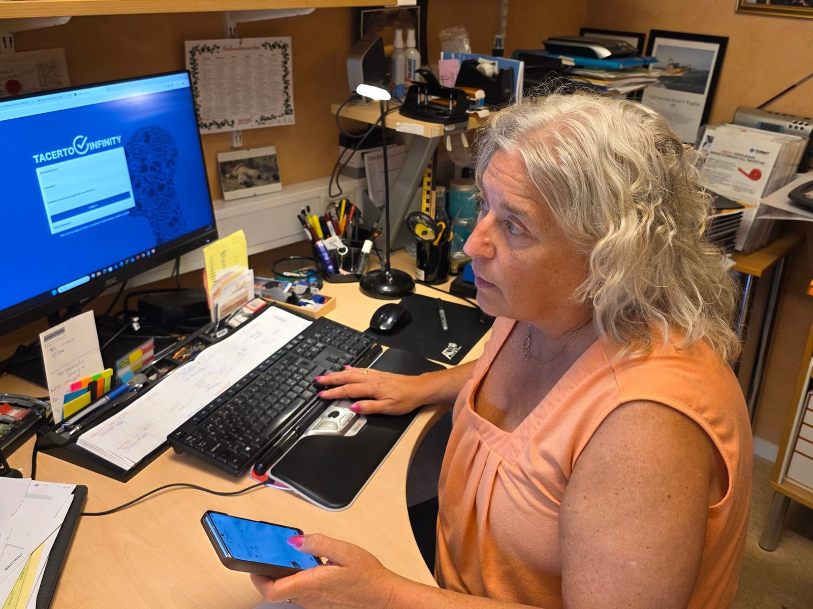 Annika Lilja vid kontorsskrivbordet med Tacerto Infinity på skärmen och mobilen i handen